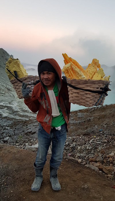 Estrazione di zolfo a Kawah Ijen: un minatore che trasporta due grandi cesti carichi di zolfo. I minatori esperti trasportano spesso carichi di zolfo che superano significativamente il loro peso corporeo.
