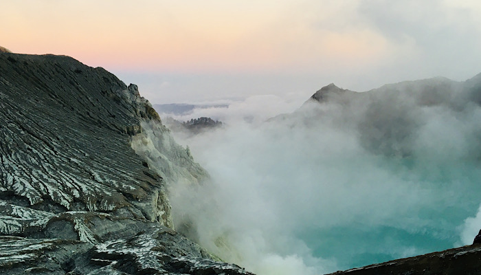 Lago acido: la luce del mattino illumina il lago della caldera color turchese sul vulcano Kawah Ijen. Un pennacchio bianco segna la posizione della solfatara, dove i gas ricchi di zolfo fuoriescono da uno sfiato. Il colore turchese dell'acqua è causato da